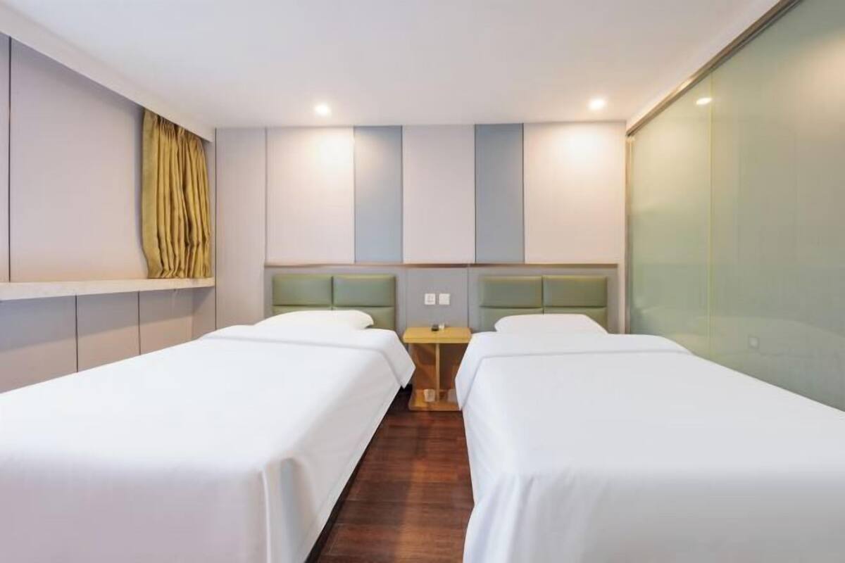 A hotel room with two single beds, a small table, and a glass partition wall.