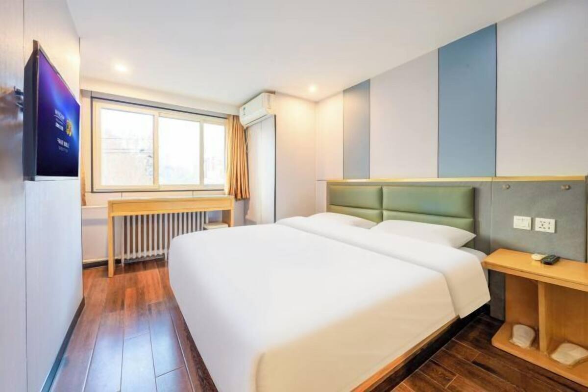 A modern hotel room with a large bed, a bedside table, a small desk, and a window with curtains.