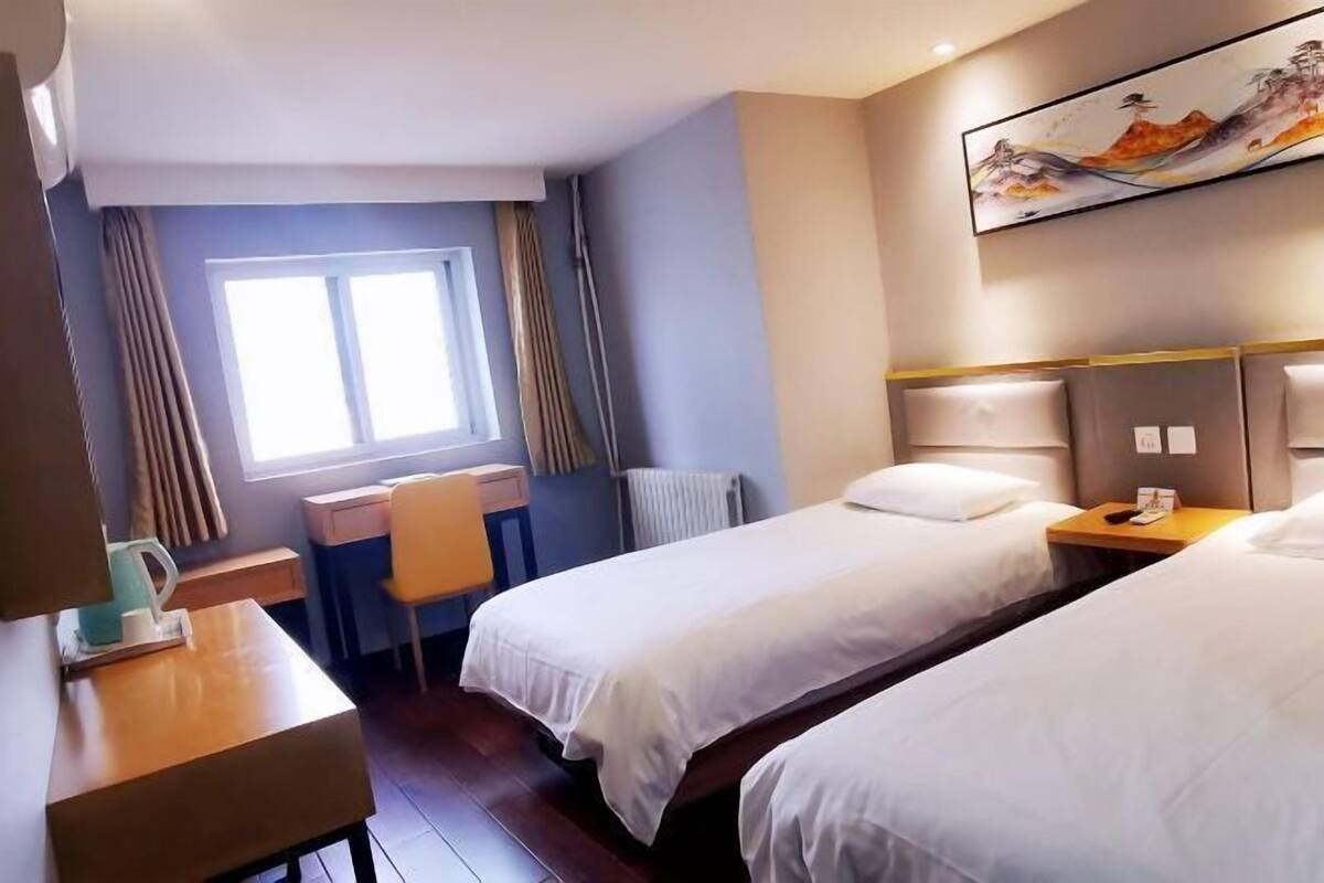 A hotel room with two beds, a desk, a chair, and a window with curtains.