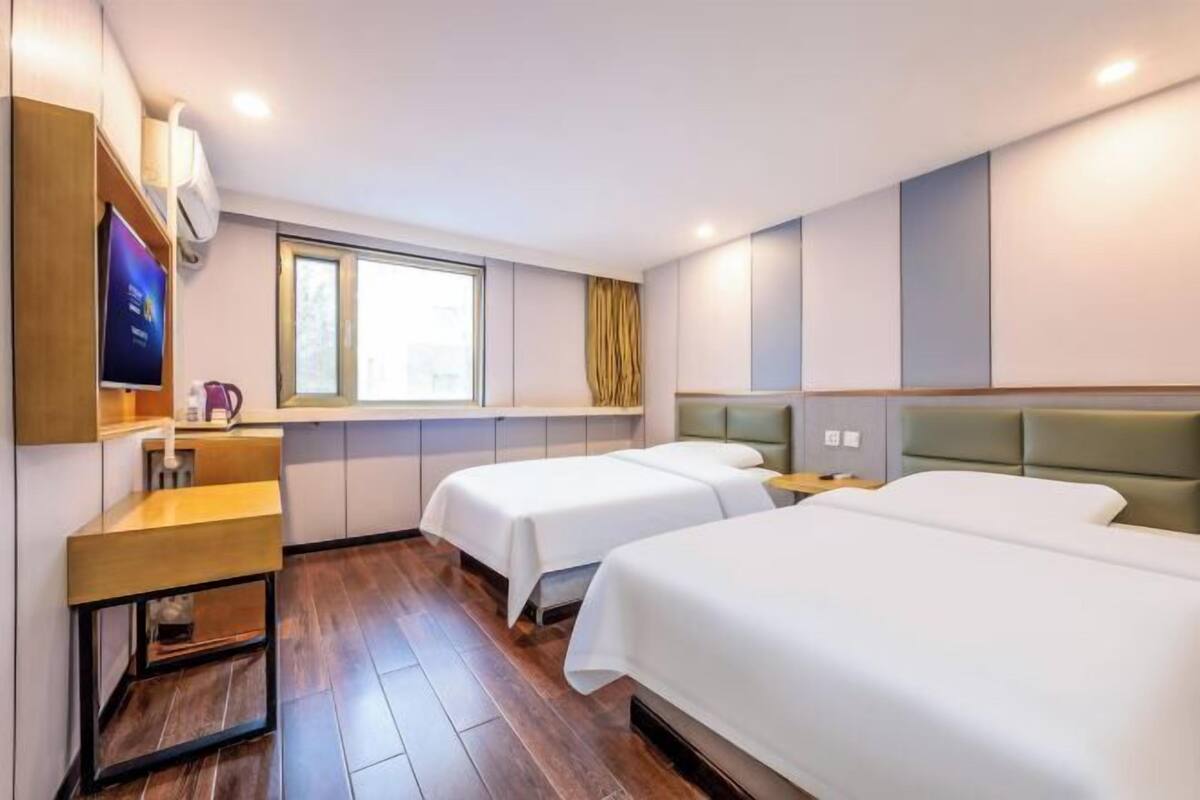 A hotel room with two beds, a wooden bench, a TV, a window, and a curtain.