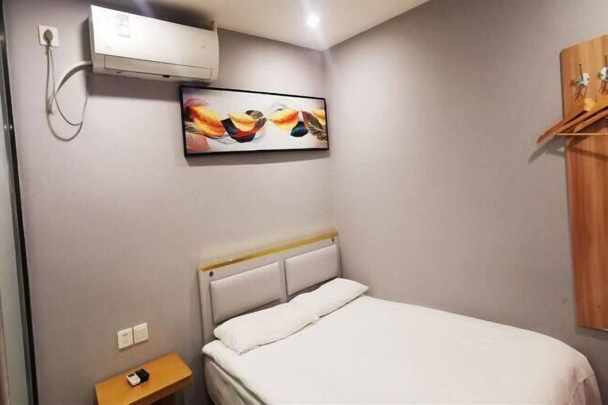 A bedroom with a bed, a bedside table, a wall-mounted air conditioner, and a painting.