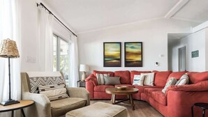A living room with a red sofa, beige armchair, and ottoman, a round wooden coffee table, and a floor lamp. - Wake & Lake - Sleeps 8, Big Water Views! + More! (Sparta)