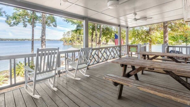 A covered outdoor area with wooden benches and chairs, overlooking a body of water with trees and an American flag. - Wake & Lake - Sleeps 8, Big Water Views! + More! (Sparta)