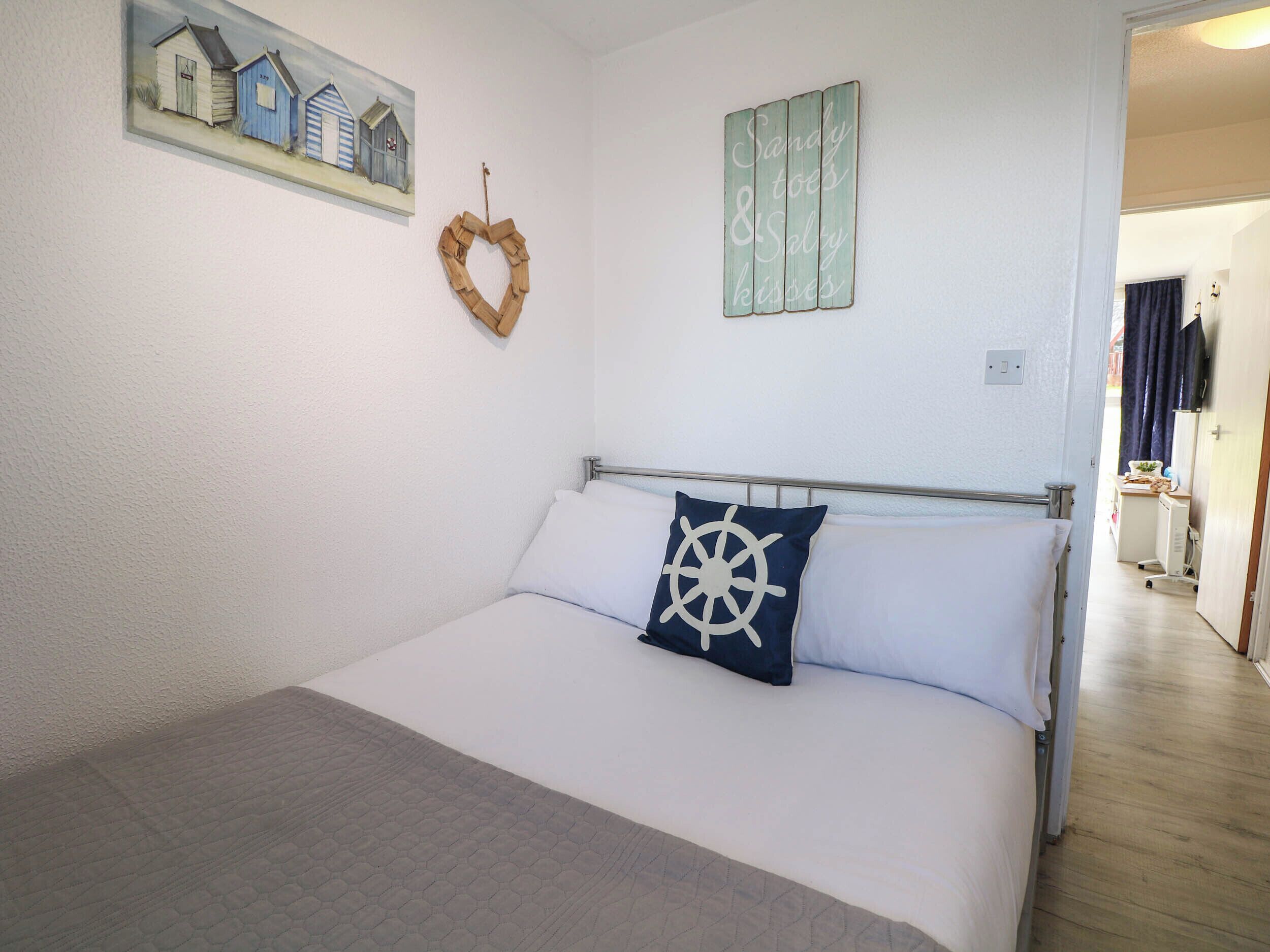 Quarto com cama, coração decorativo na parede e arte decorativa com tema náutico.