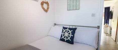 Quarto com cama, coração decorativo na parede e arte decorativa com tema náutico.