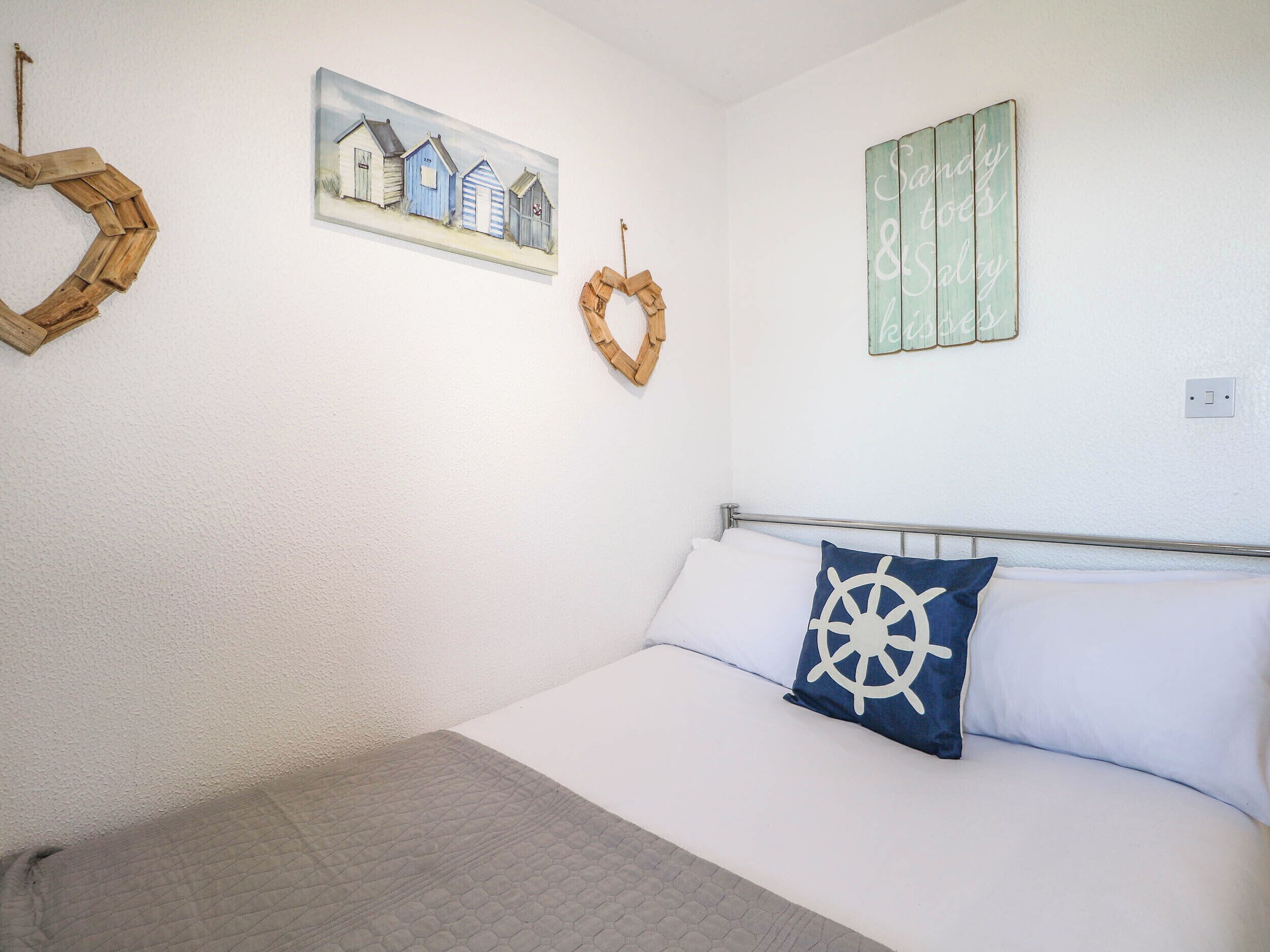 Quarto com cama, pintura de cabanas na praia, decoração de coração de madeira e um letreiro com texto.