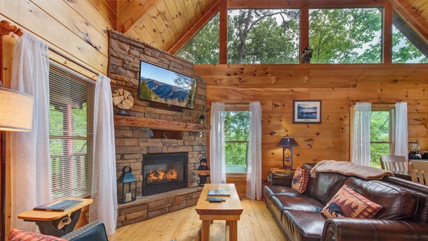 A cozy cabin interior with a fireplace, wooden walls, a leather sofa, and a dining area.