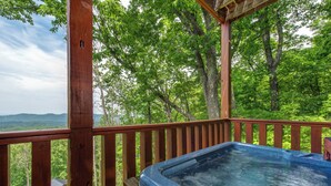A hot tub on a wooden deck with a view of a forest and mountains.