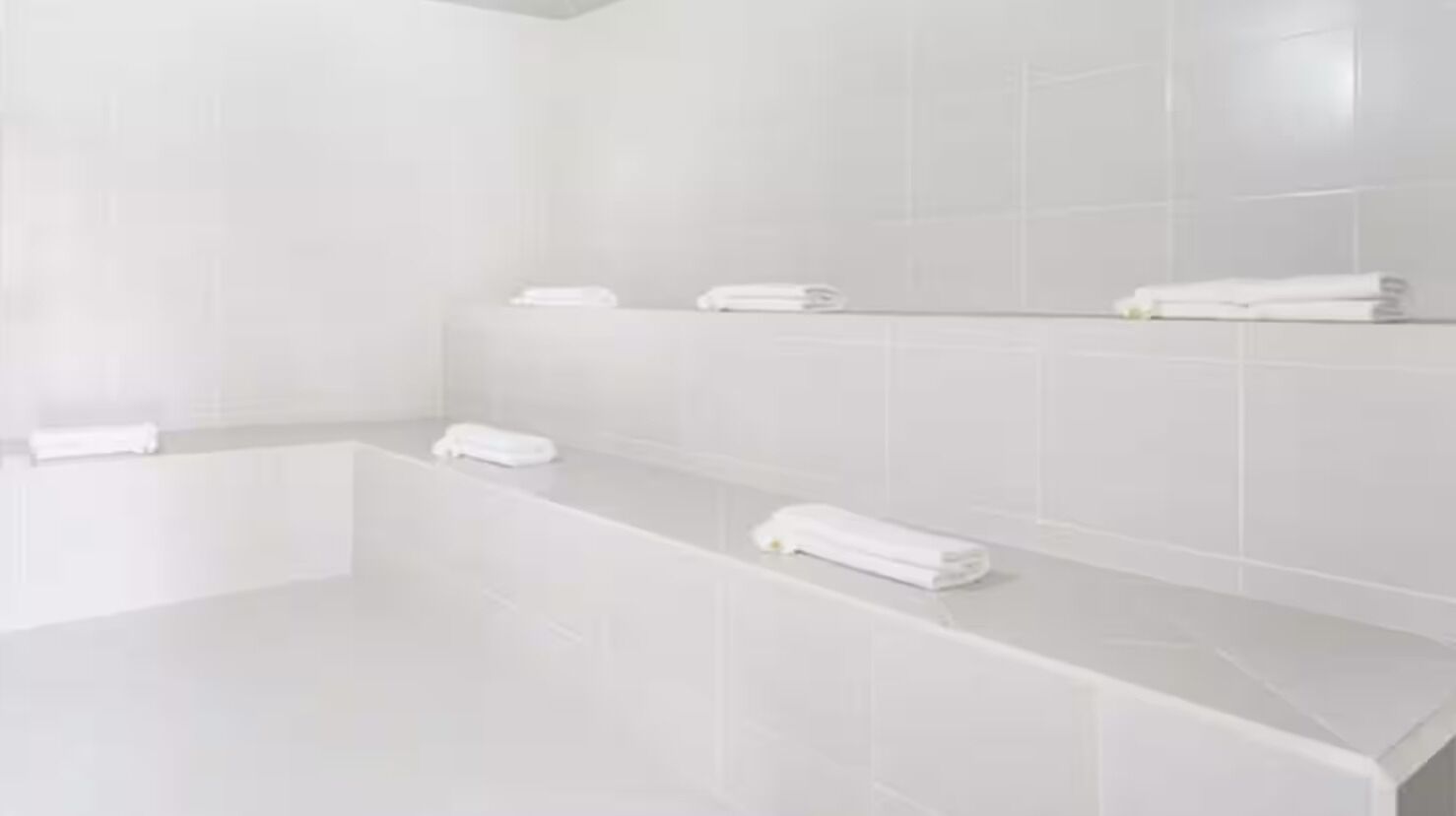 A modern bathroom with white tiles, a bathtub, and neatly arranged towels on a shelf.
