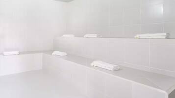 A modern bathroom with white tiles, a bathtub, and neatly arranged towels on a shelf.
