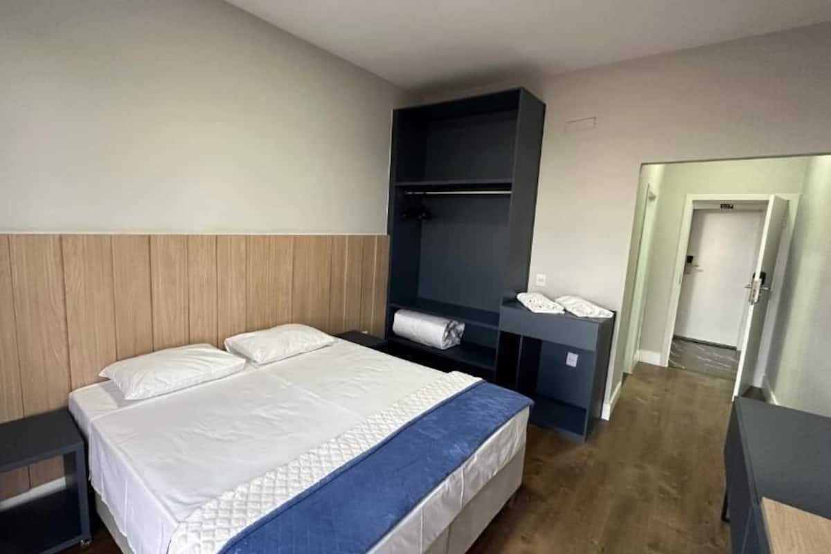 A hotel room with a bed, a bedside table, a wardrobe, and a door leading to another room.