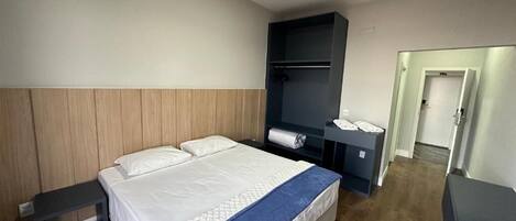 Una habitación de hotel con cama, mesita de noche, armario y puerta que da a otra habitación.