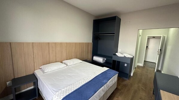 A hotel room with a bed, a bedside table, a wardrobe, and a door leading to another room. - Hotel Colibri (Viçosa)