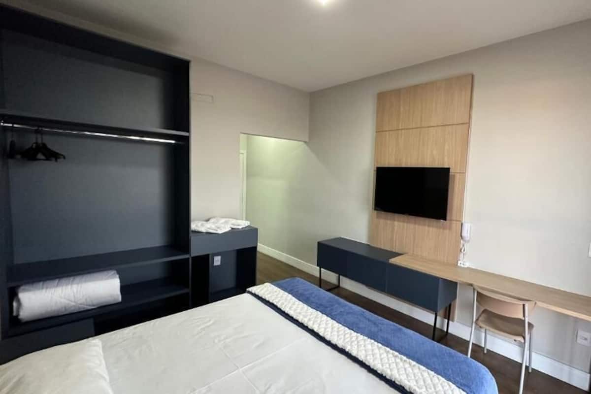 A modern hotel room with a bed, a desk, a TV, and built-in storage.