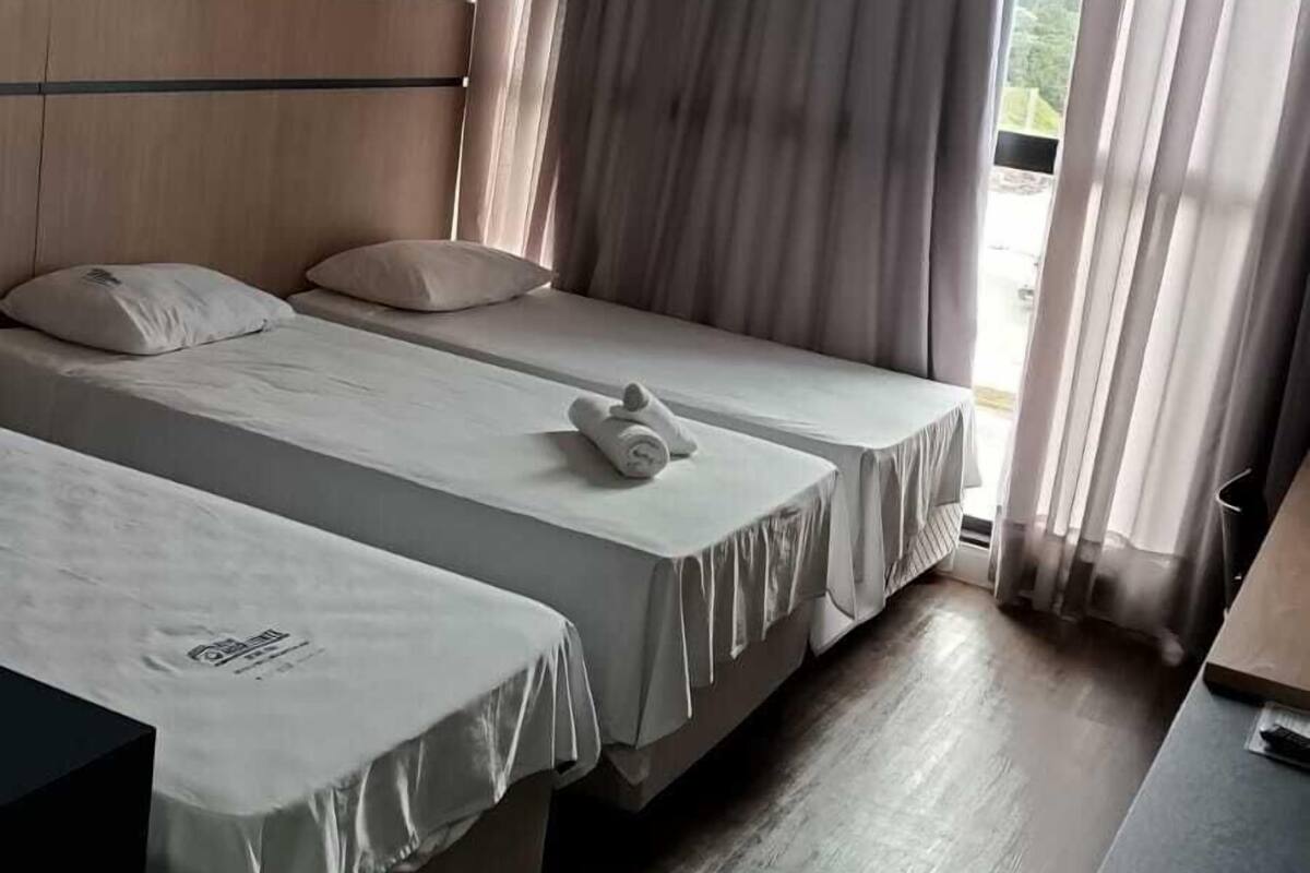 A hotel room with two beds, a wooden headboard, a desk, and a window with curtains.