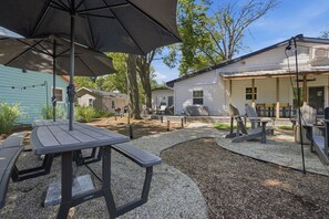 A patio with picnic tables and an umbrella, surrounded by houses.