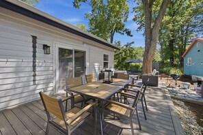 A wooden deck with a table and chairs, a grill, and a covered area with a table and chairs. - Union Pier Cottage Close To Everything! One Of Three Units! (Union Pier)