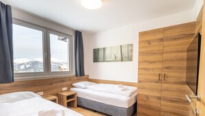A hotel room with two beds, a large window with a view, a painting on the wall, and wooden furniture. - Apartment in Katschberghohe Near Ski Slopes (Rennweg am Katschberg)