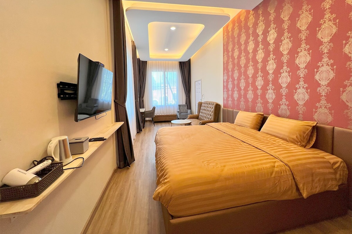 Ein Hotelzimmer mit einem großen Bett, einem an der Wand montierten Fernseher, einem Schreibtisch mit Stuhl und einem Fenster mit Vorhängen.