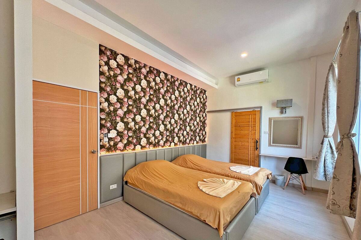 Ein Schlafzimmer mit zwei Betten, einem Holzschrank, einer Wandverkleidung mit Blumenmuster, einem Spiegel und einer Klimaanlage.