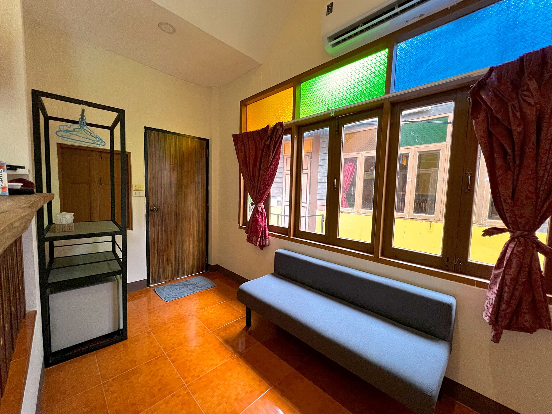 Una habitación con un banco, una puerta de madera, una ventana con cortinas y un suelo de baldosas.