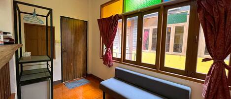 Una habitación con un banco, una puerta de madera, una ventana con cortinas y un suelo de baldosas.