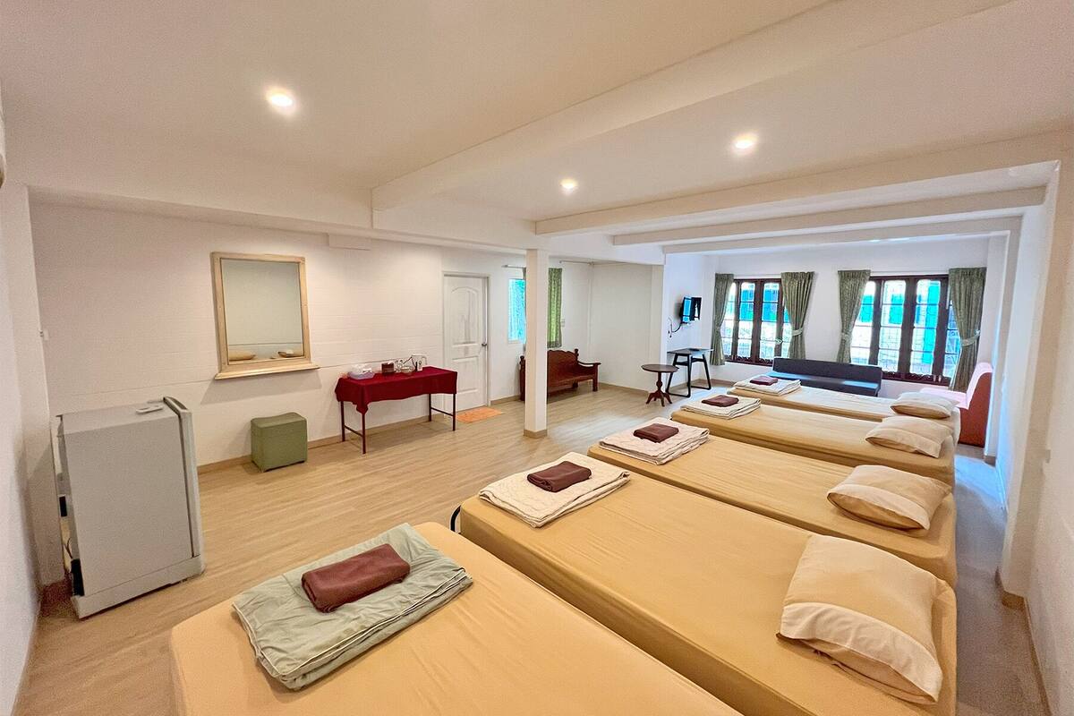 Ein Hotelzimmer mit mehreren Betten, einem Schreibtisch, einem Stuhl, einem Spiegel und einem Fernseher.