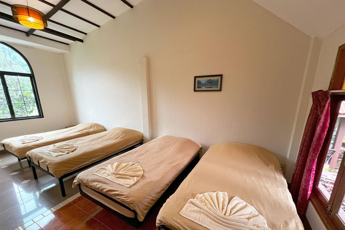 Ein Zimmer mit drei Einzelbetten, einem Fenster mit Blick und einem kleinen gerahmten Bild an der Wand.