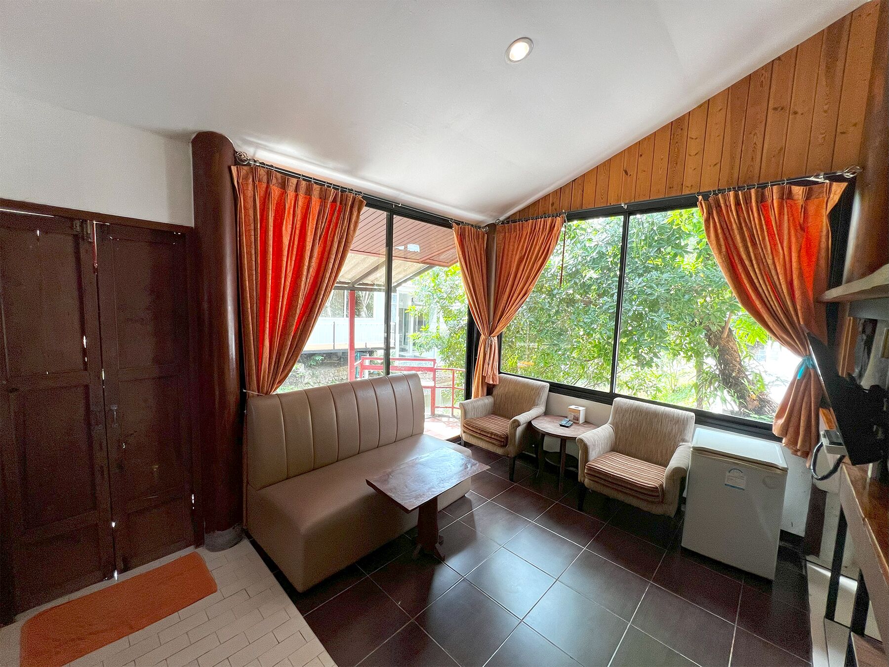 A room with a sofa, two armchairs, a small table, and a refrigerator.