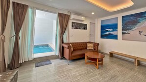 A living room with a sofa, coffee table, and a view of the ocean through large windows. - Phuiyara Resort Nakhonnayok (Nakhon Nayok)
