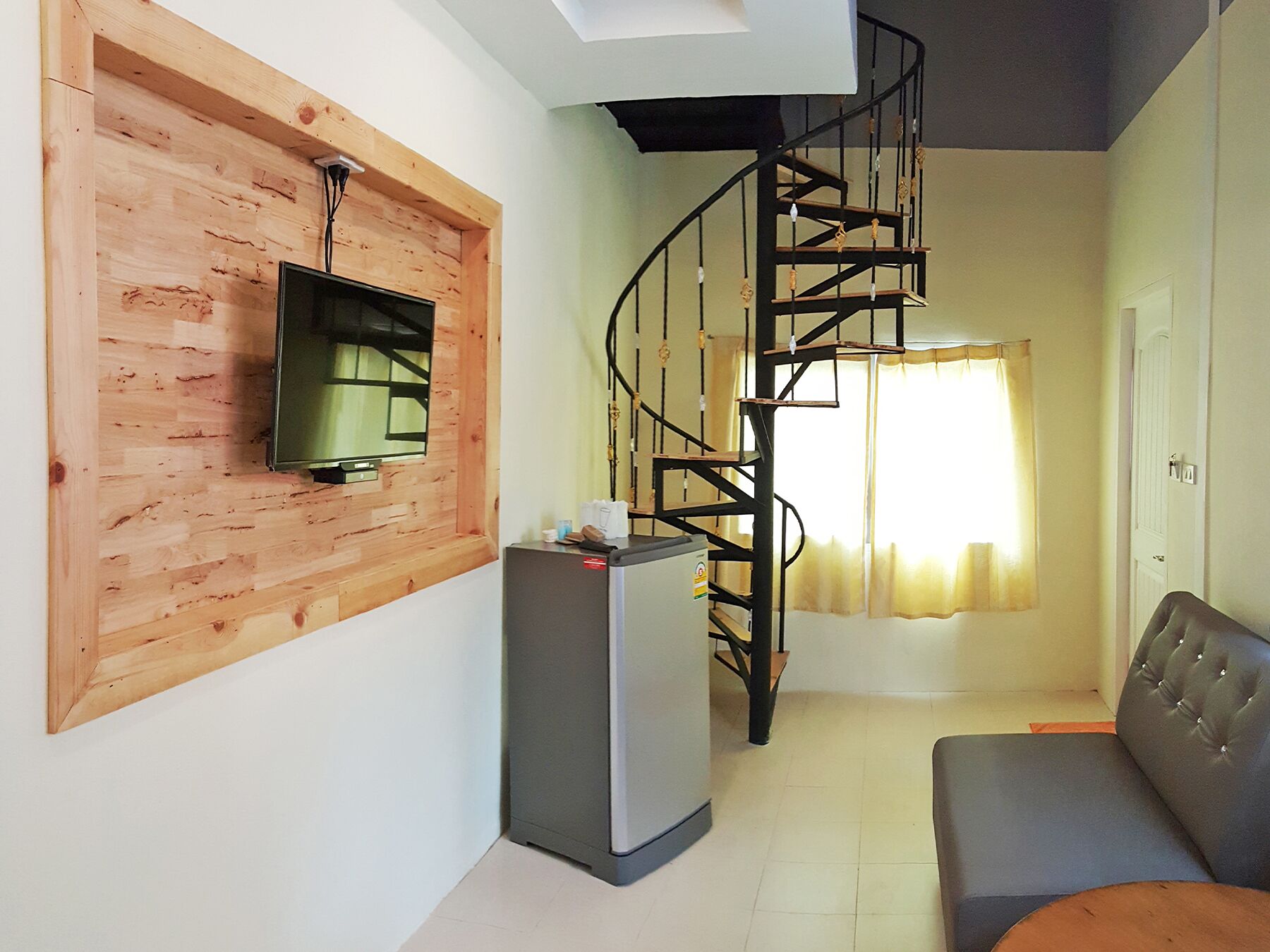 Un espacio habitable compacto con una pared de madera, un televisor de pantalla plana, un refrigerador, una escalera de caracol y un sofá.