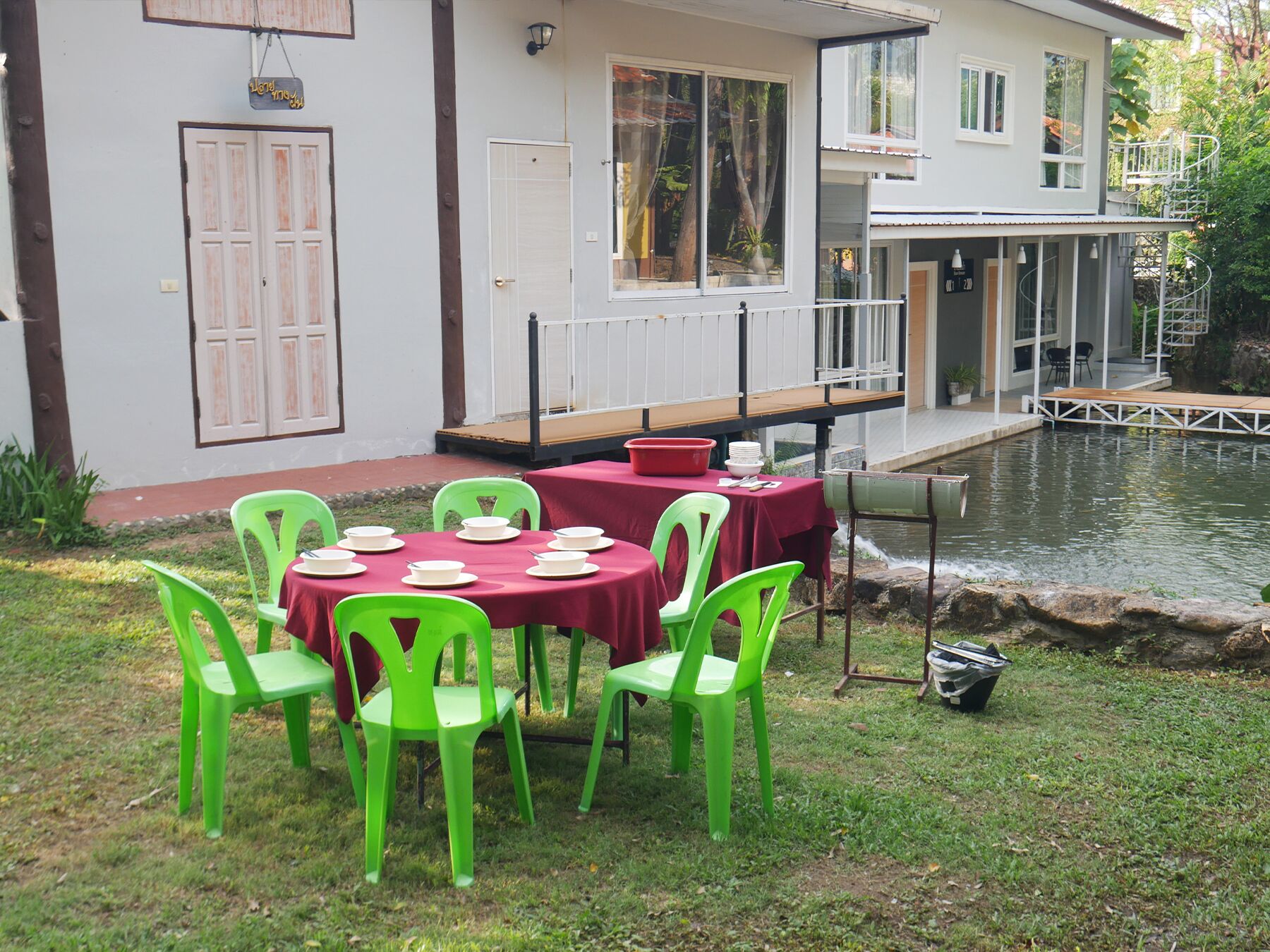 Un comedor con mesas redondas y sillas verdes, un pequeño estanque y un edificio con ventanas amplias y un balcón.