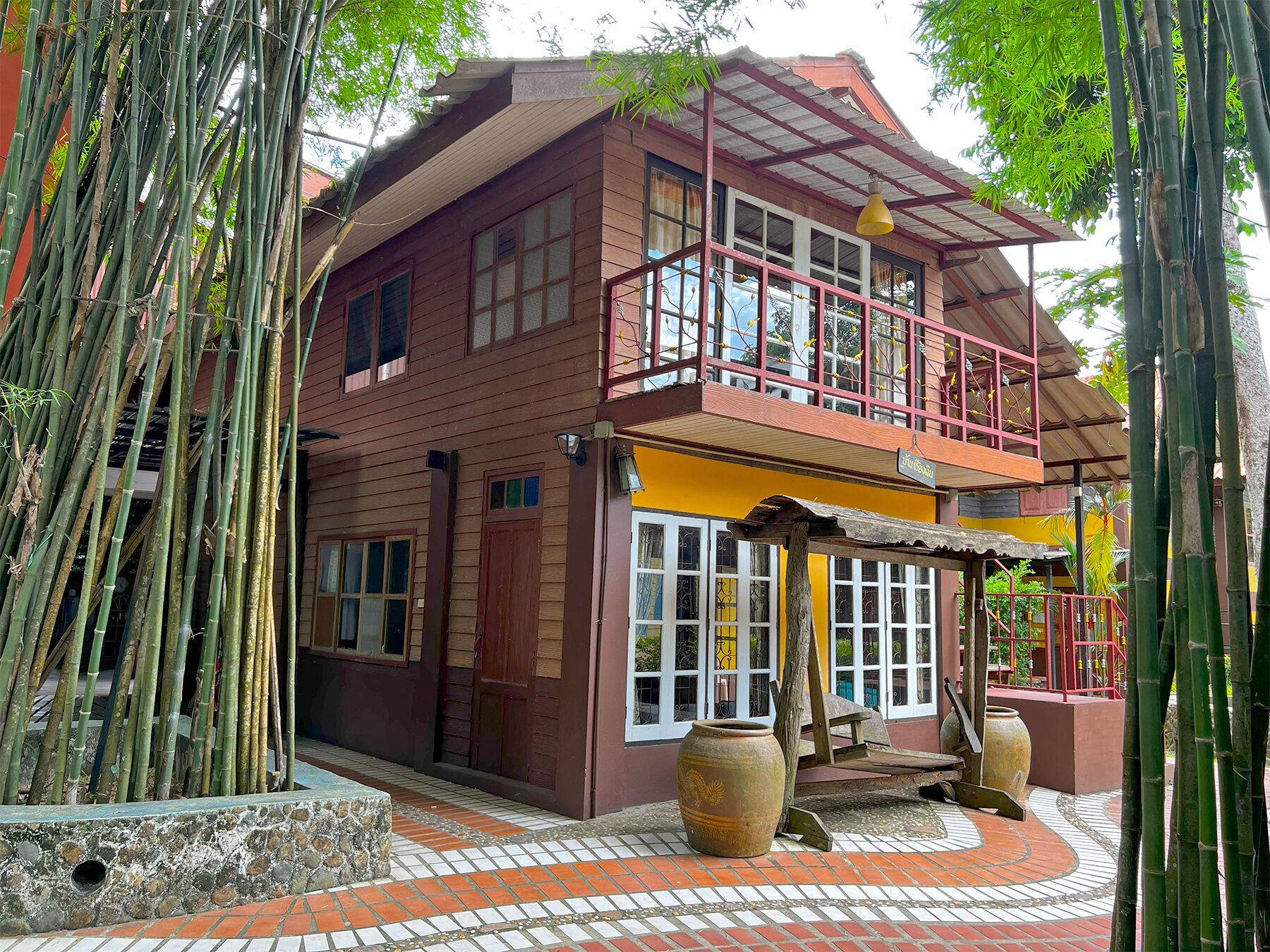 A two-story building with a balcony, large windows, and a tiled patio area with decorative vases.
