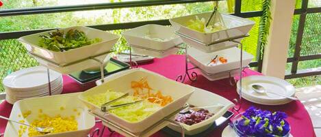 Ein reichhaltiges Buffet mit verschiedenen Speisen und Geschirr, draußen mit Blick ins Grüne.
