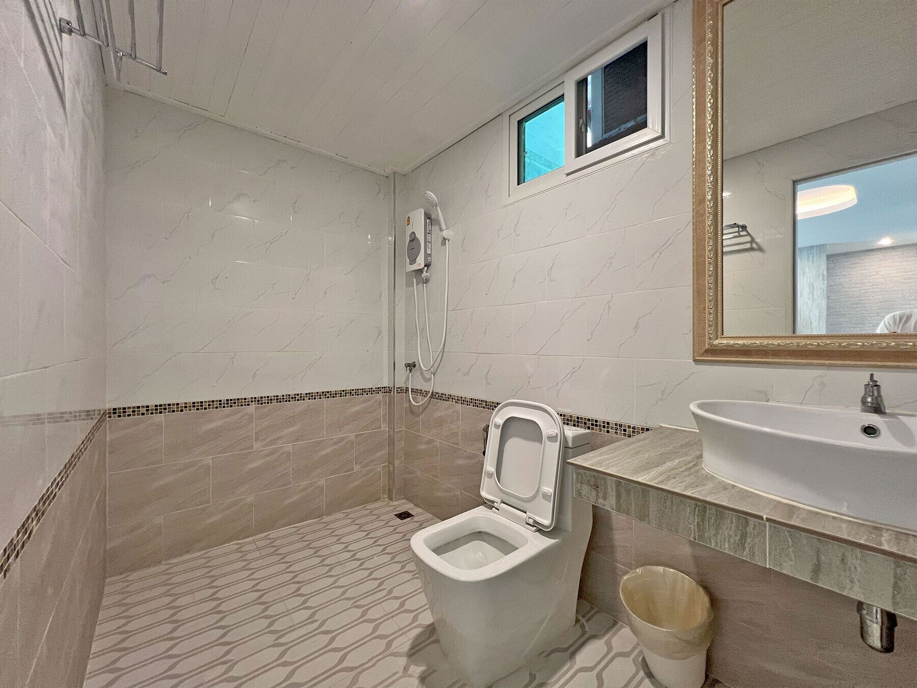 A bathroom with a toilet, shower, sink, and a small window.