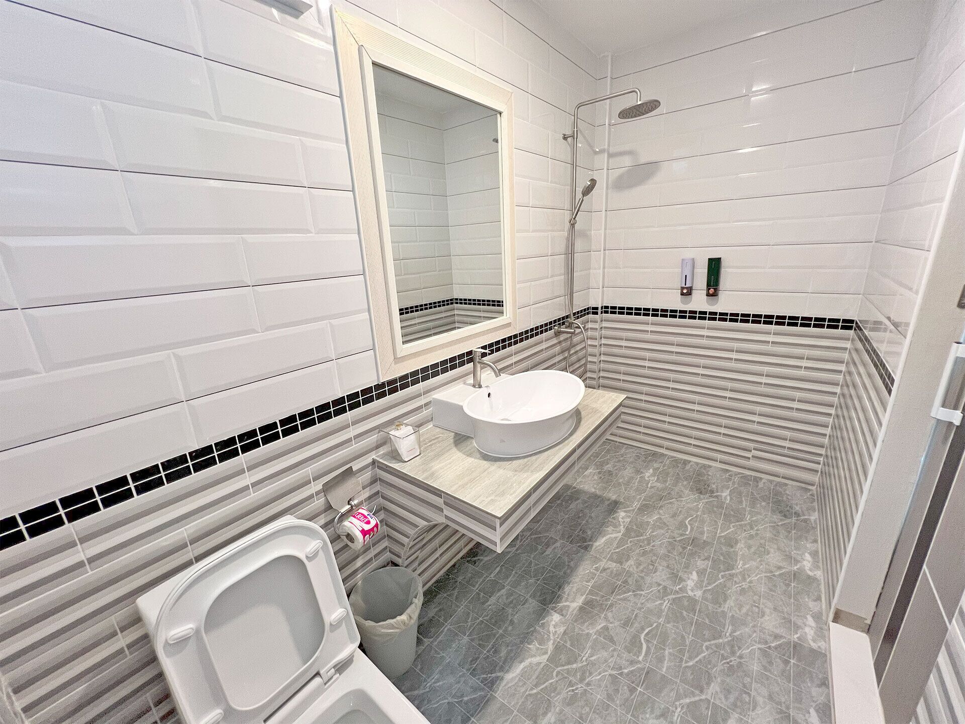A bathroom with white subway tiles, a round sink, a toilet, and a shower area.