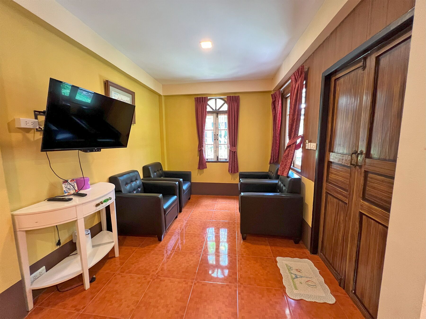 A living room with a flat-screen TV, two black leather sofas, a white side table, and a wooden door.