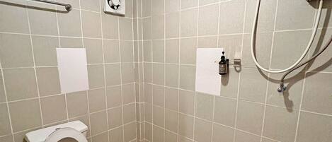 A bathroom with two toilets, a shower, and a hand dryer.