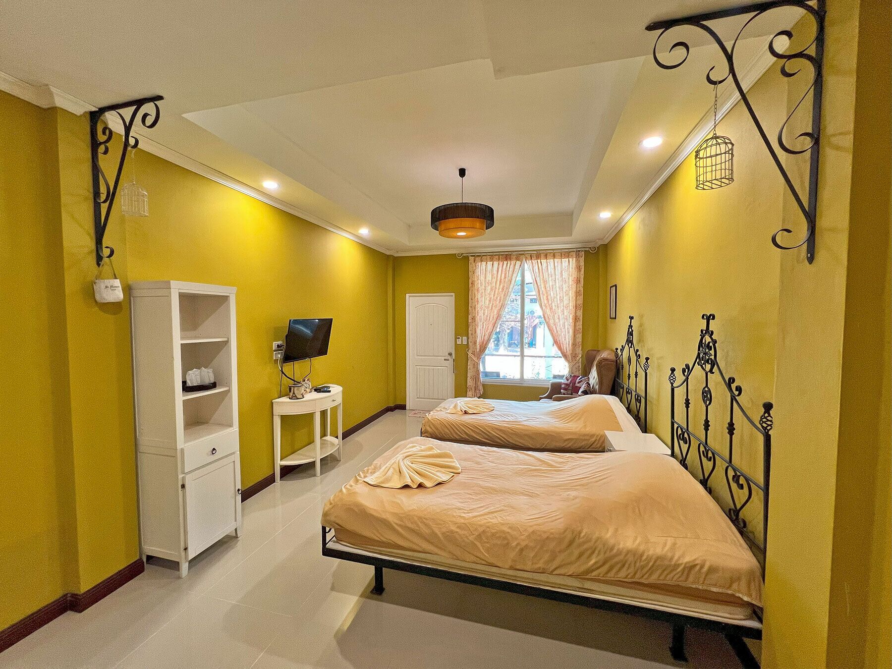 Une chambre avec deux lits, une télévision, une armoire et une fenêtre avec des rideaux.