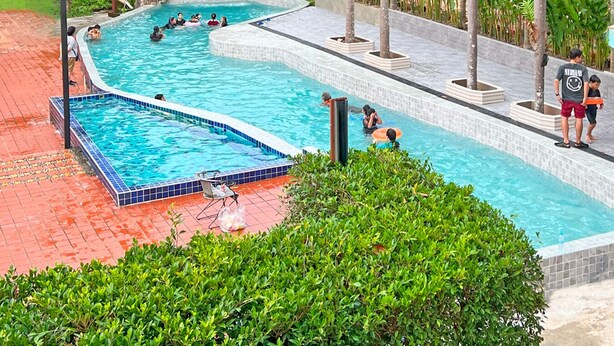 A swimming pool with a waterfall feature, surrounded by lush greenery and palm trees. - Phuiyara Resort Nakhonnayok (Nakhon Nayok)