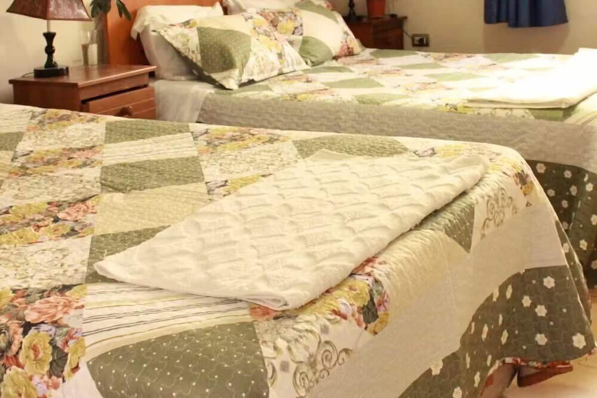 Quarto com duas camas, cada uma com colcha florida, uma mesa de cabeceira com abajur e decoração de borboletas na parede.