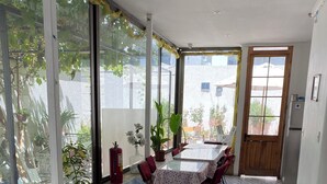 A spacious room with a large window, a dining area with a table and chairs, a sofa with a patterned throw, and a refrigerator. - Hotel El Rinconcito Acogedor (Santiago)
