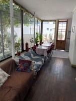 A spacious room with a large window, a dining area with a table and chairs, a sofa with a patterned throw, and a refrigerator.