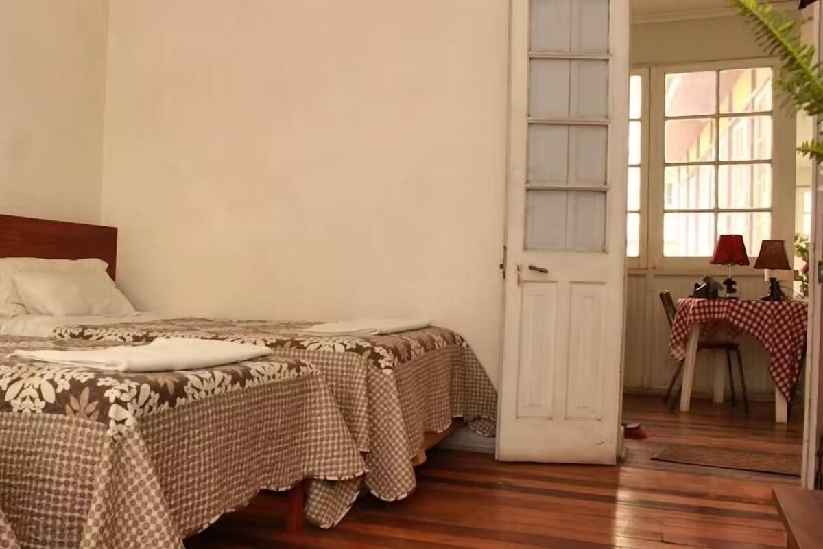 Quarto com cama de madeira, colcha xadrez e decoração floral na parede.