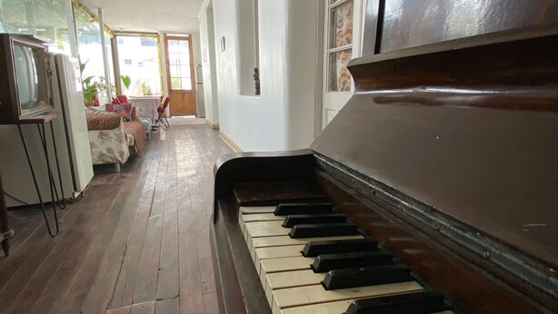A piano in a spacious room with a tiled floor and a view of a dining area. - Hotel El Rinconcito Acogedor (Santiago)