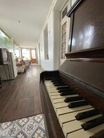 A piano in a spacious room with a tiled floor and a view of a dining area.