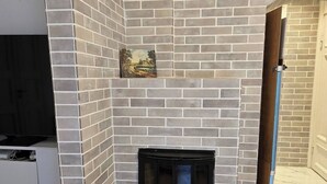 A fireplace with a brick surround, a television on a stand, and a cross on the wall. - H21A-Central-Cozy Spacious Suits family-3 rooms (Oslo)