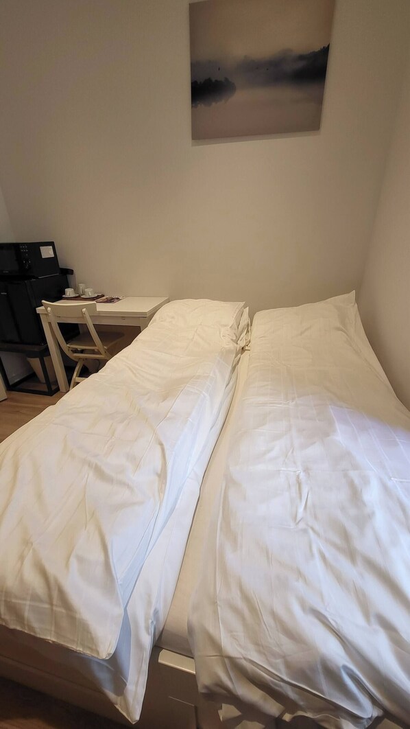 A bed with white linens, a desk with a computer, and a painting on the wall.