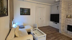Uma sala de estar moderna com um sofá branco, uma mesa de centro de vidro, uma televisão de tela plana e uma lareira de tijolos.