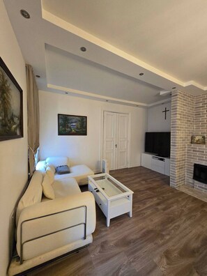 Una sala de estar moderna con un sofá blanco, una mesa de centro de vidrio, un televisor de pantalla plana y una chimenea de ladrillo.